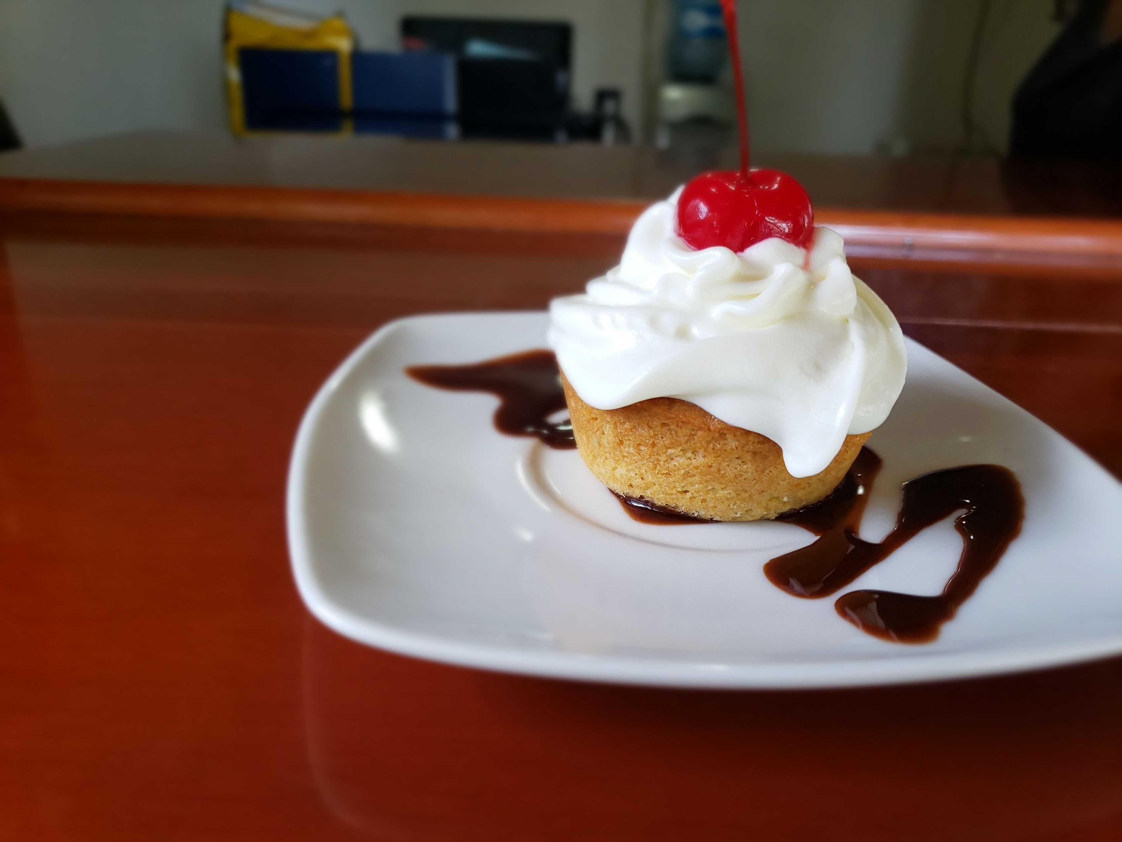 A dessert on a white plate with a cherry on top, surrounded by chocolate sauce.