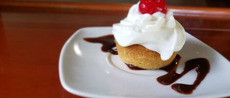A dessert on a white plate with a cherry on top, surrounded by chocolate sauce.