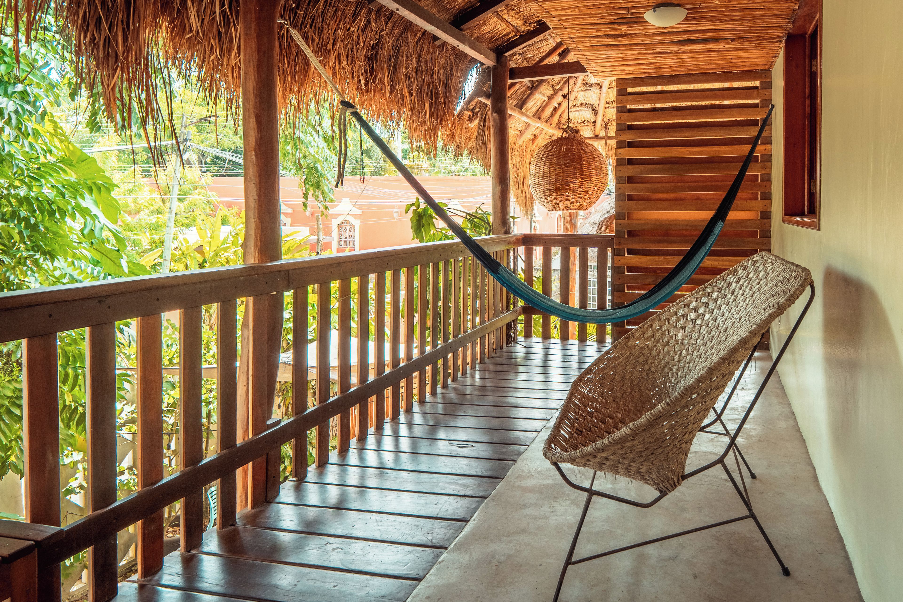 Un balcon en bois surmonté d’un toit de chaume, un hamac tressé et une chaise en osier.