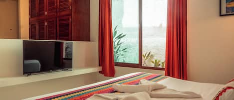 A hotel room with a bed, a television, a window with curtains, and a wall-mounted cabinet.