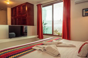 Una habitación de hotel con cama, televisión, ventana con cortinas y un mueble fijado a la pared.