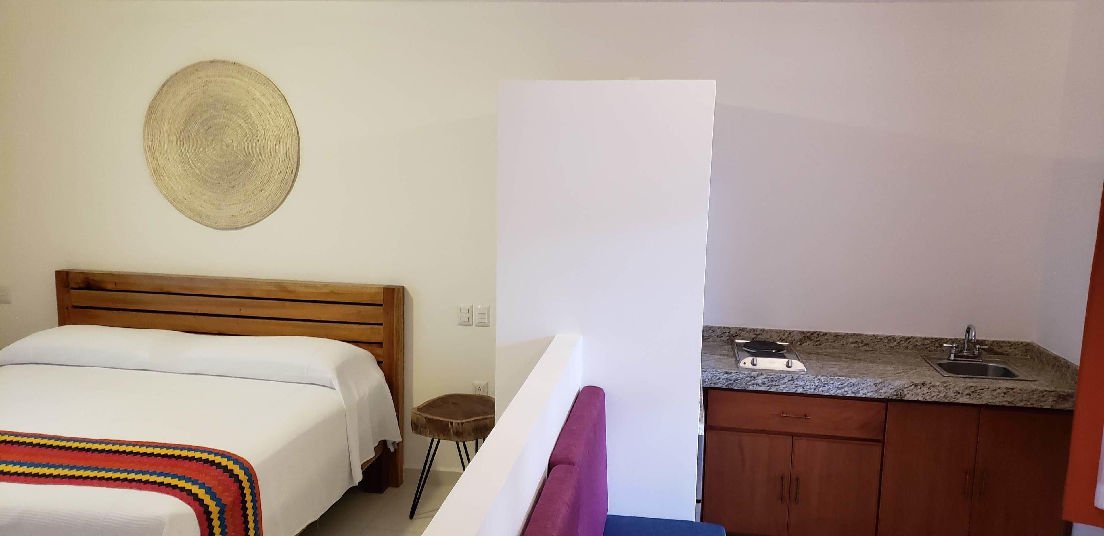 Un dormitorio con cama de madera, un taburete pequeño y una cocina con encimera de granito y lavamanos.