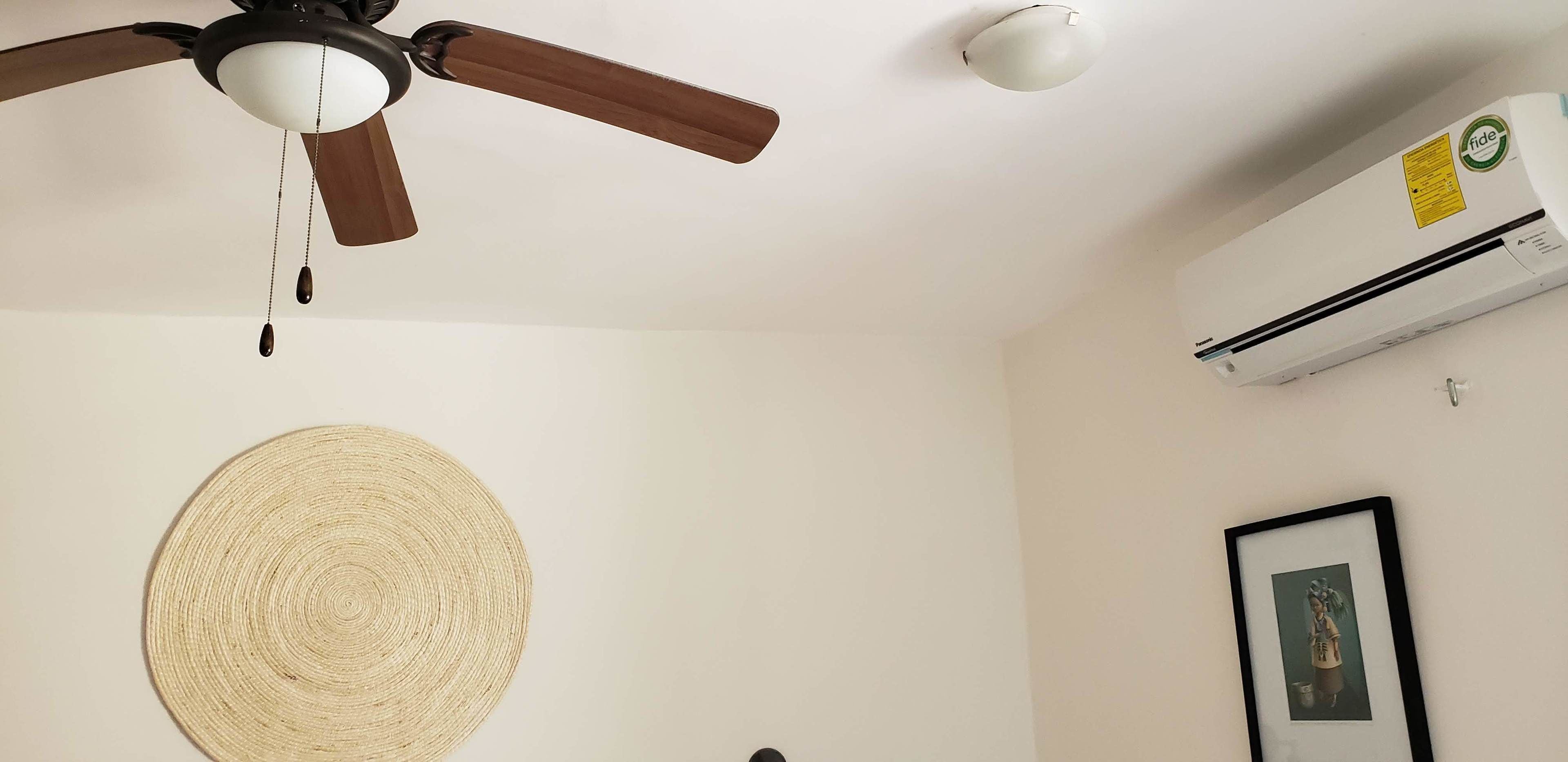 Un ventilateur de plafond, un détecteur de fumée et un appareil de climatisation dans une pièce.