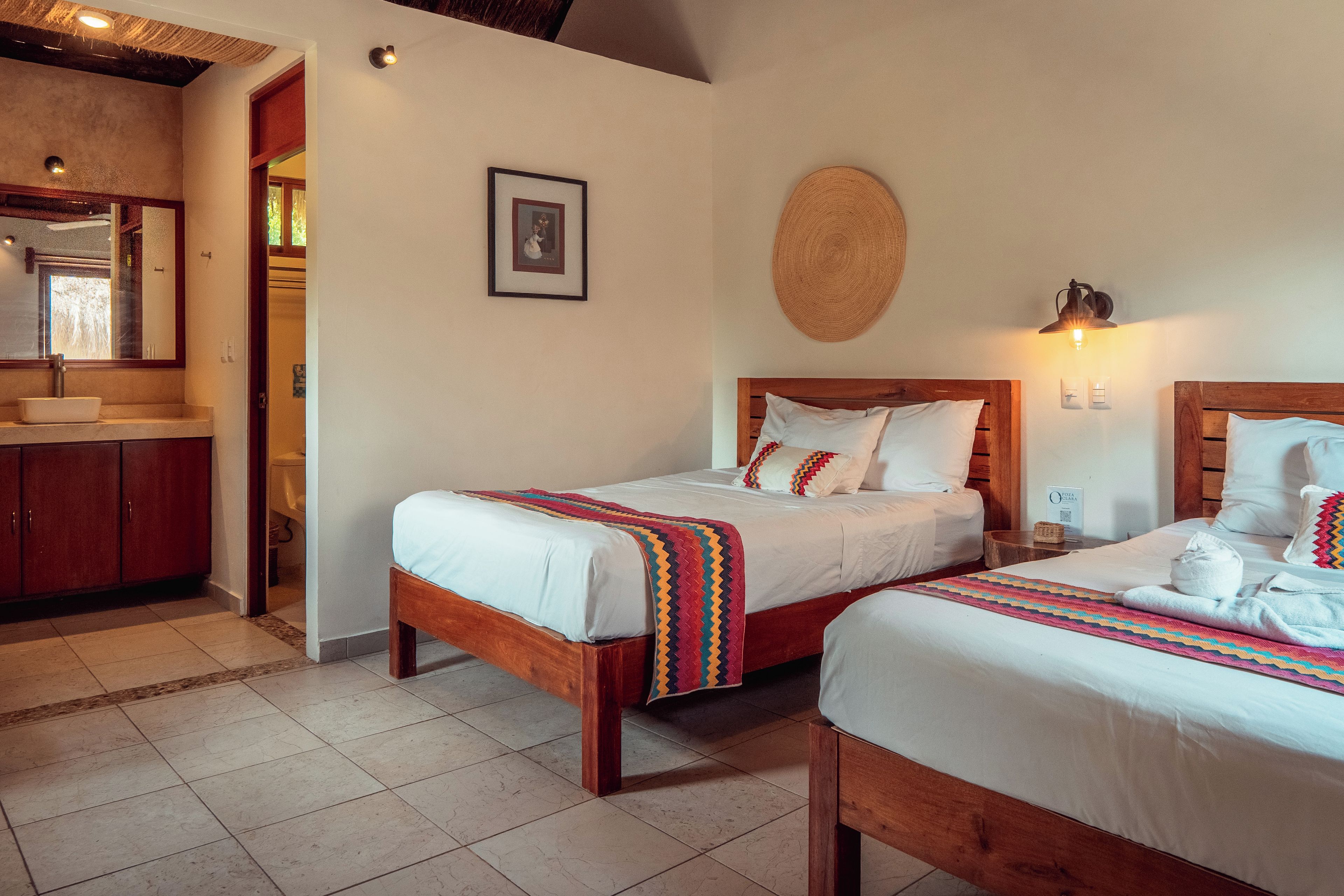 Een hotelkamer met twee houten bedden, een badkamer met een grote spiegel en een kitchenette.
