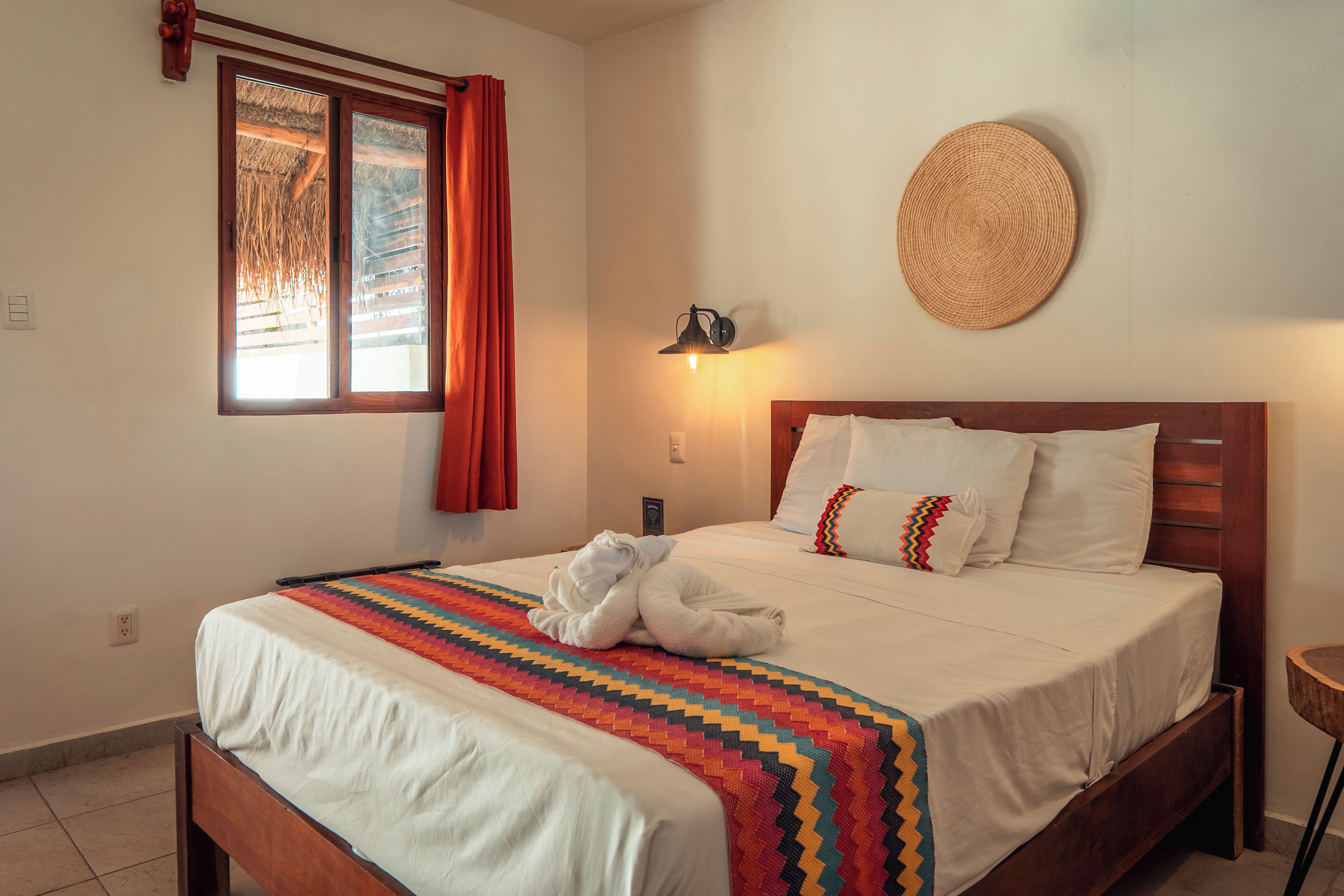 Ein Hotelzimmer mit Bett, einem fensterbelaubten Fenster, einer Wandlampe und einer gewobenen Wanddekoration.