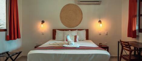 Una habitación de hotel con cama, dos lámparas de noche, aire acondicionado de pared y una mesa de comedor con sillas.
