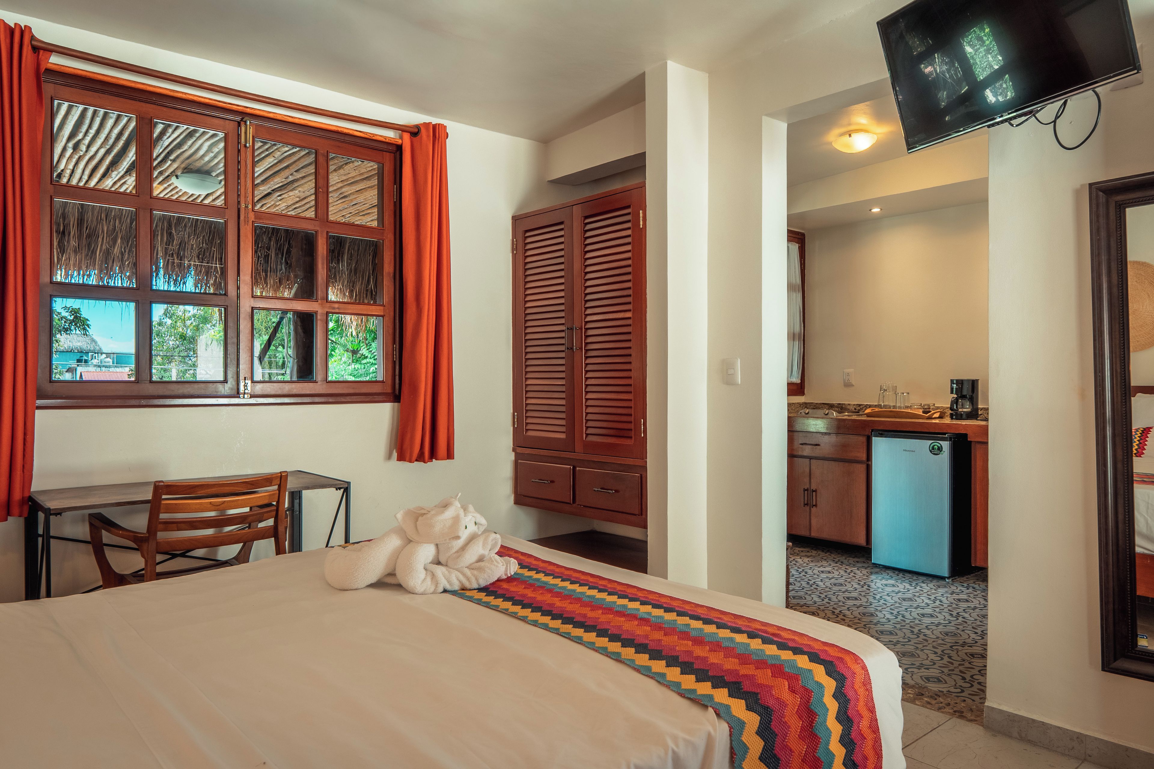 Habitación de hotel con cama, escritorio, silla, televisión y kitchenette.