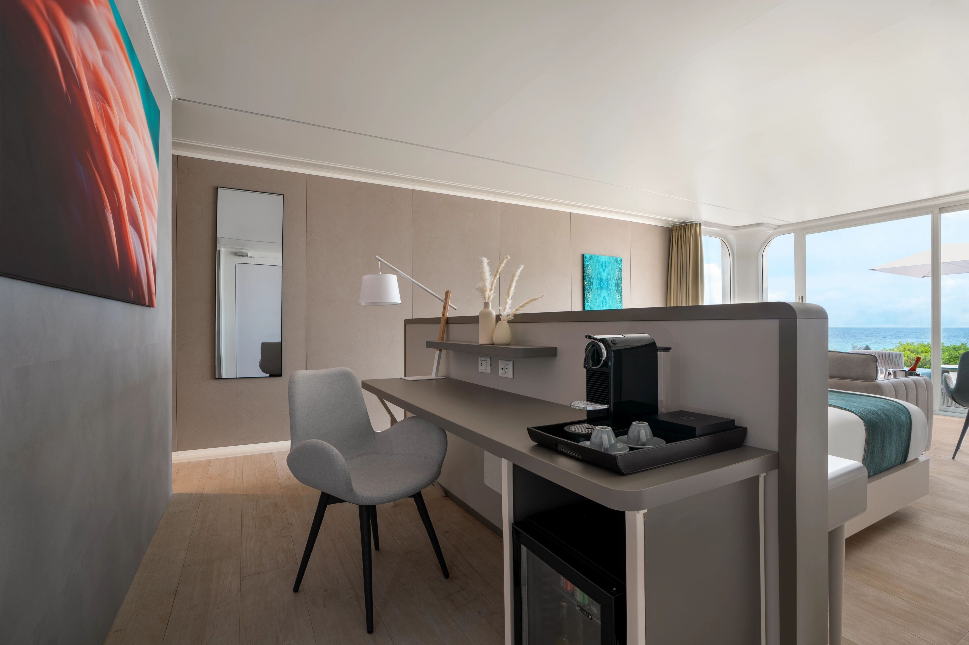 A modern hotel room with a kitchenette, a dining area, and a large window offering a view of the sea.