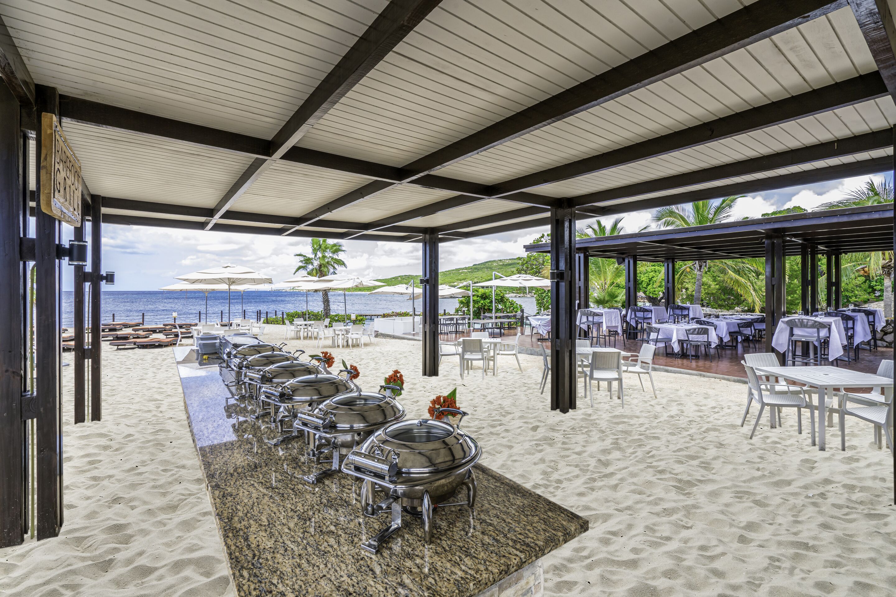 A covered outdoor dining area with a beach view, including a buffet setup and seating arrangements.