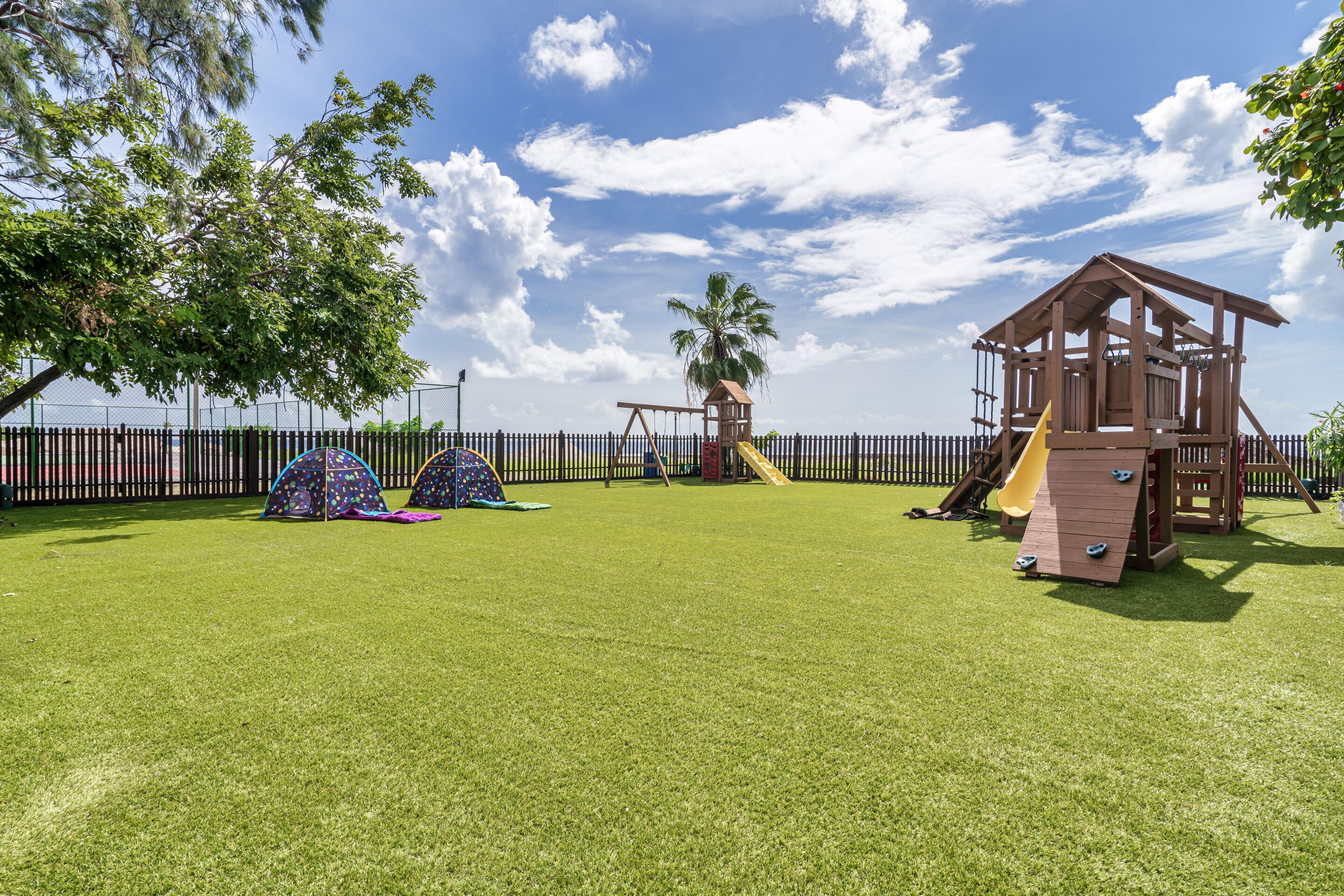 A playground with a wooden playhouse, slides, and tents.