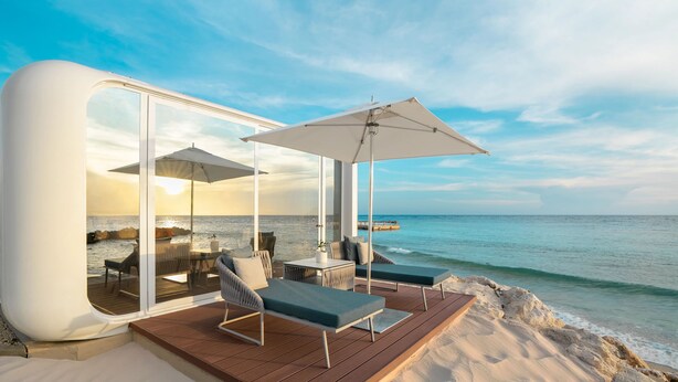 Una villa moderna sulla spiaggia, con veranda vetrata, mobili da esterno e vista sull'oceano.