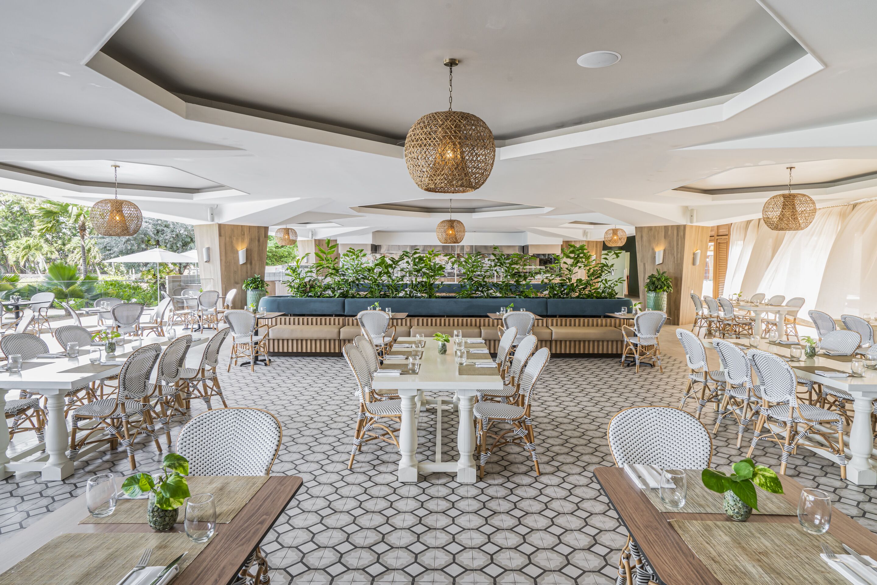 A spacious outdoor dining area with multiple tables and chairs, surrounded by lush greenery and a patterned floor.