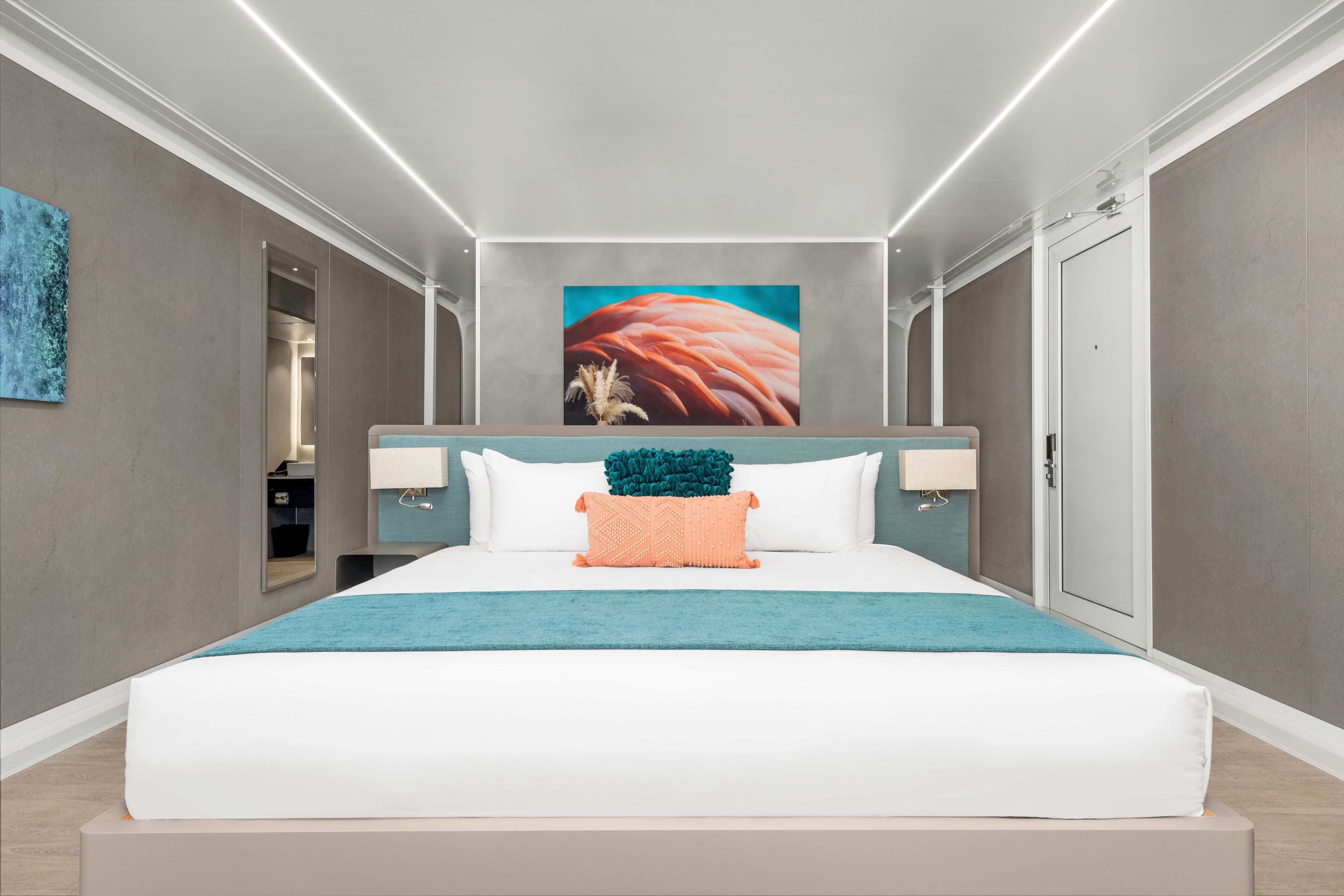 A modern hotel room with a large bed, a teal throw blanket, and a large painting on the wall.