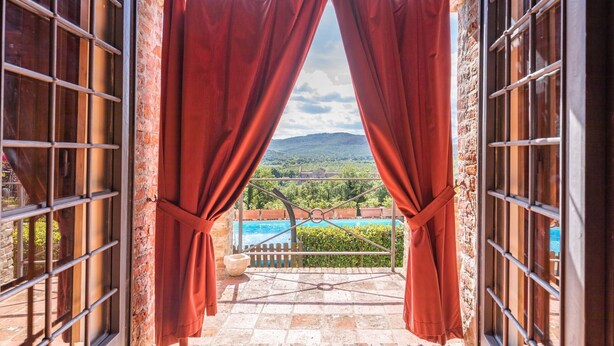 An open doorway with red curtains, leading to a pool area with a view of a mountainous landscape.