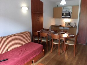 Un espace de vie compact comprenant un canapé, une table à manger, des chaises et un coin cuisine.