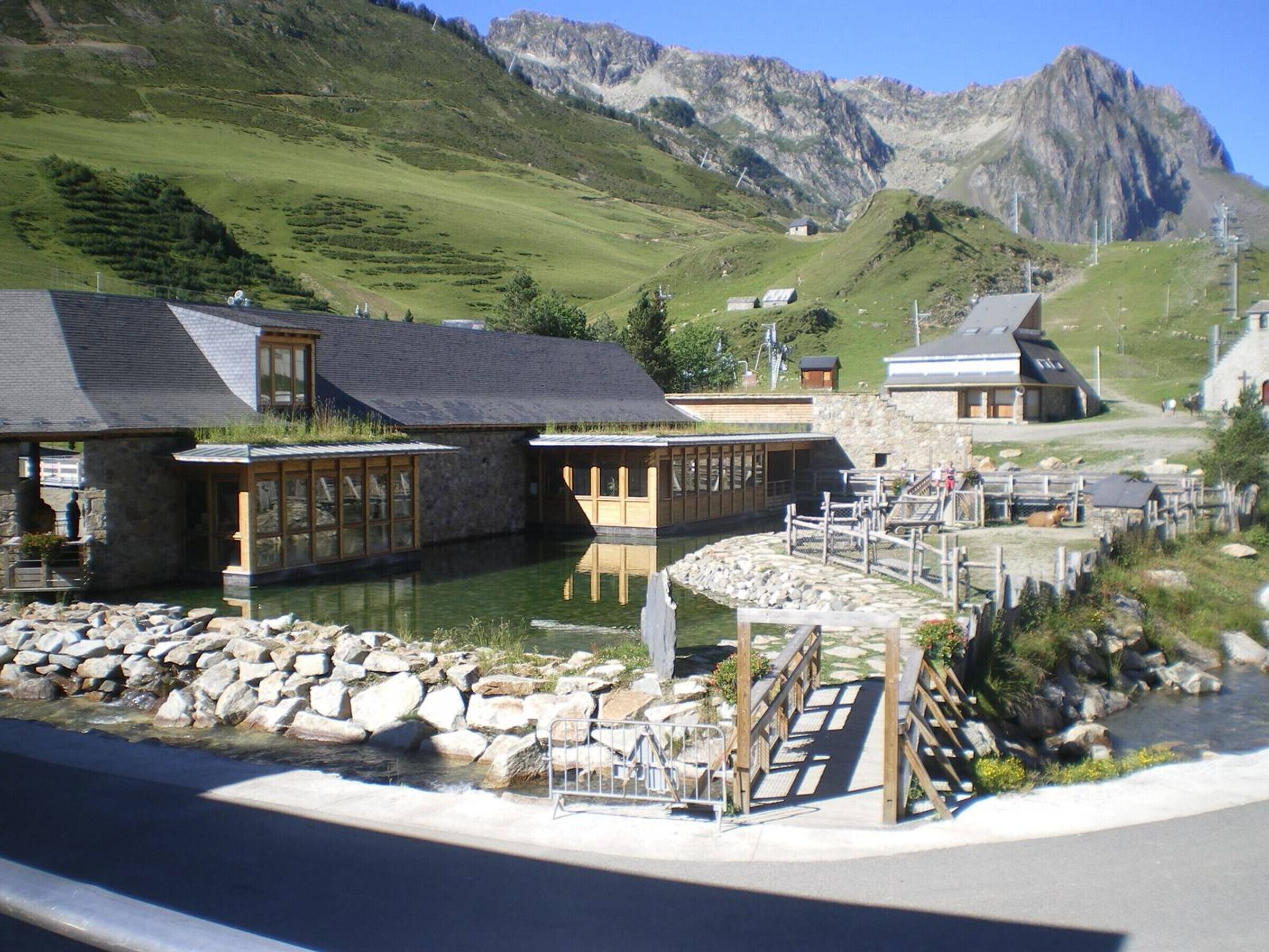 A lakeside hotel with stone buildings, a dock, and a mountain backdrop.