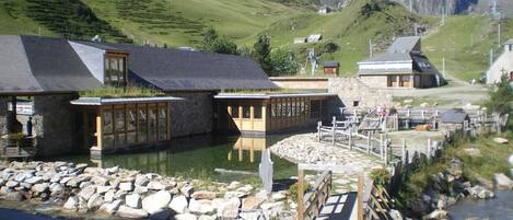 A lakeside hotel with stone buildings, a dock, and a mountain backdrop.