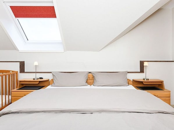 A modern bedroom with a skylight, a large bed, two bedside tables, and a wooden crib.