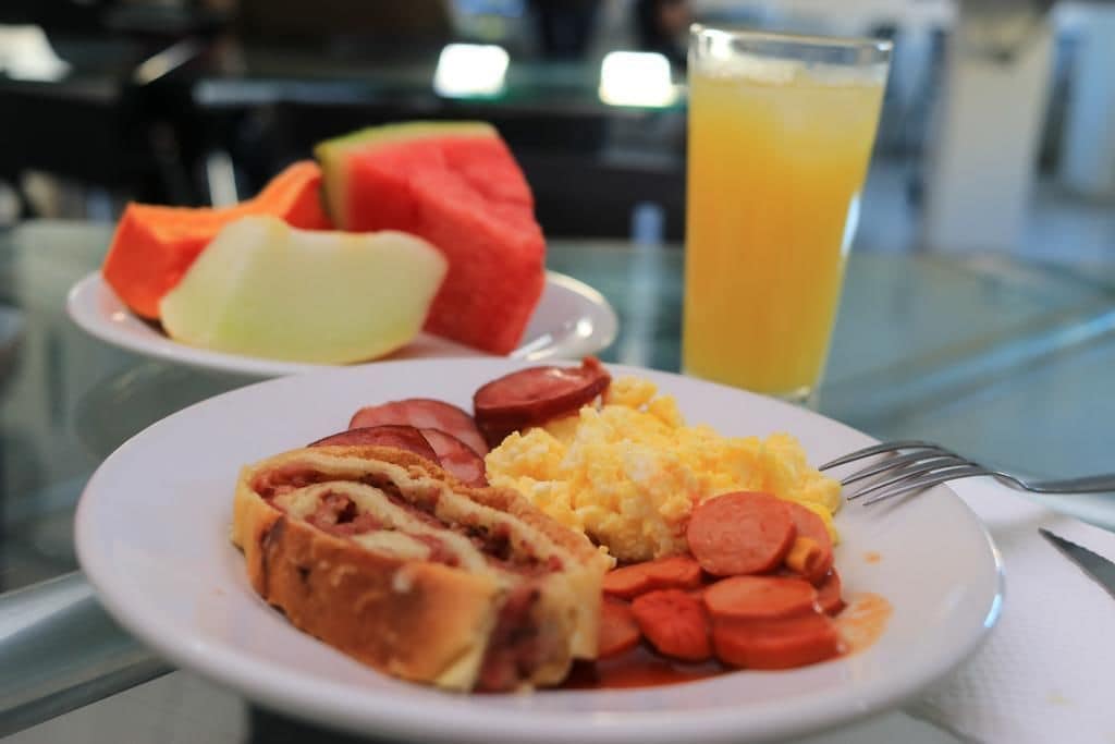 A meal with sausage, scrambled eggs, and watermelon on a plate, with a glass of orange juice in the background.