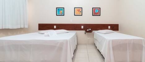 Habitación de hotel con dos camas, cabecero de madera, cortina blanca y tres cuadros en la pared.