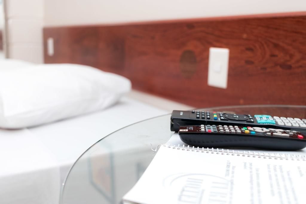 A remote control and a notebook on a glass table in a hotel room.