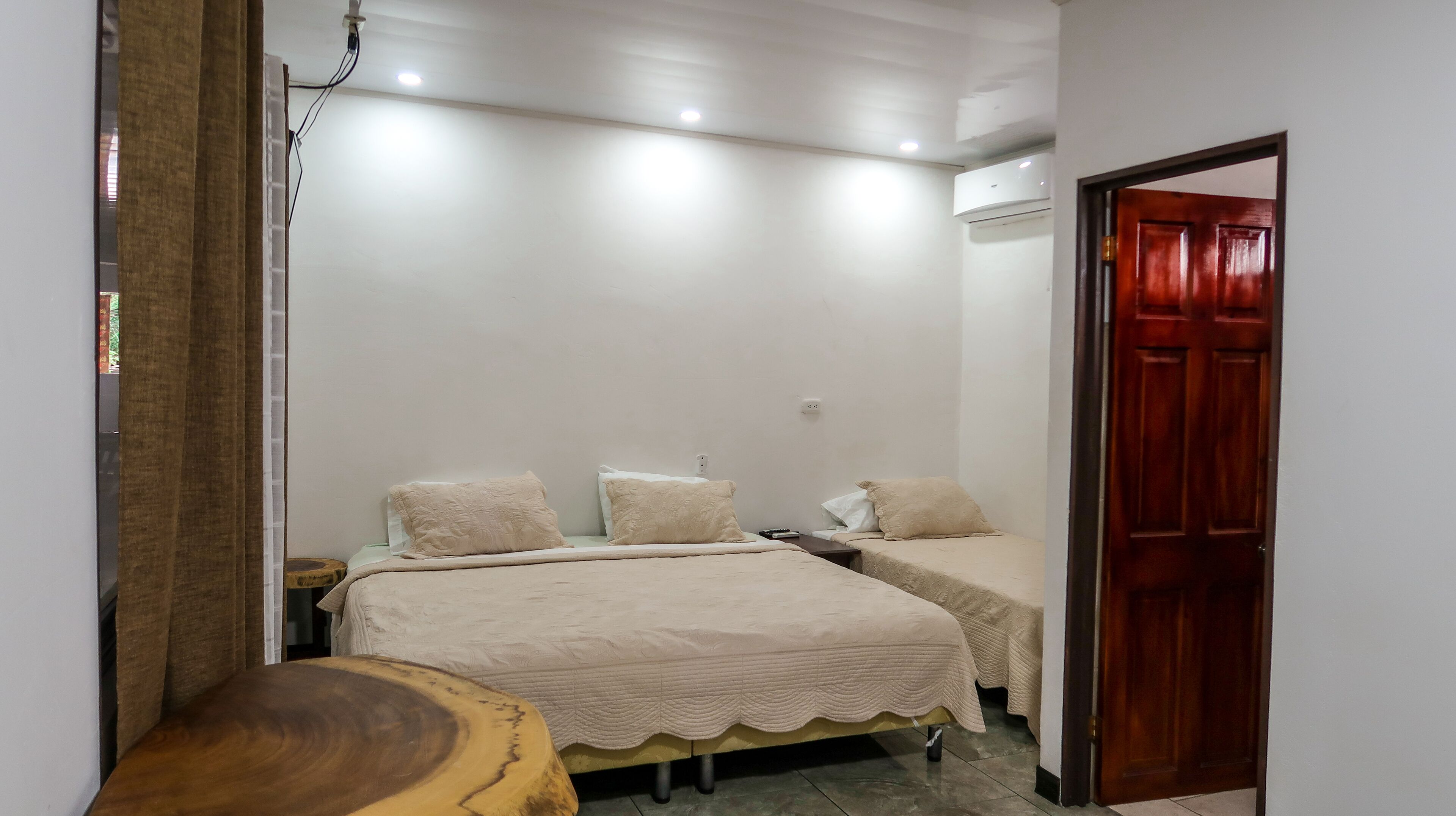 A bedroom with two beds, a wooden side table, and a door.