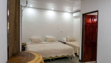 A bedroom with two beds, a wooden side table, and a door.