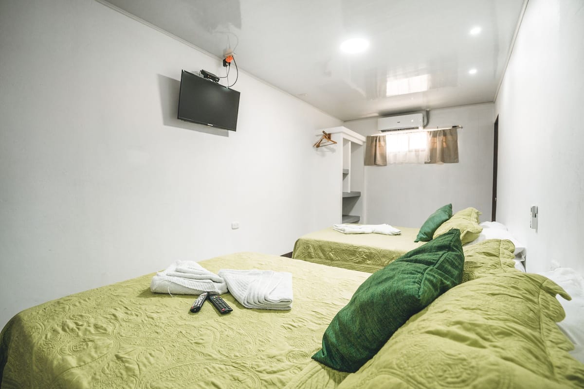 A hotel room with two beds, a flat-screen TV mounted on the wall, and a window with curtains.