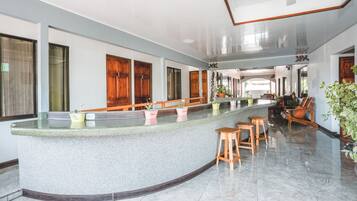 A spacious lobby with a curved reception desk, wooden doors, and seating area with chairs and potted plants.