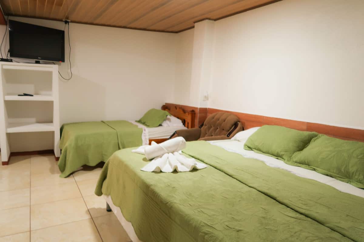 A hotel room with two beds, a TV mounted on the wall, and a shelf unit.