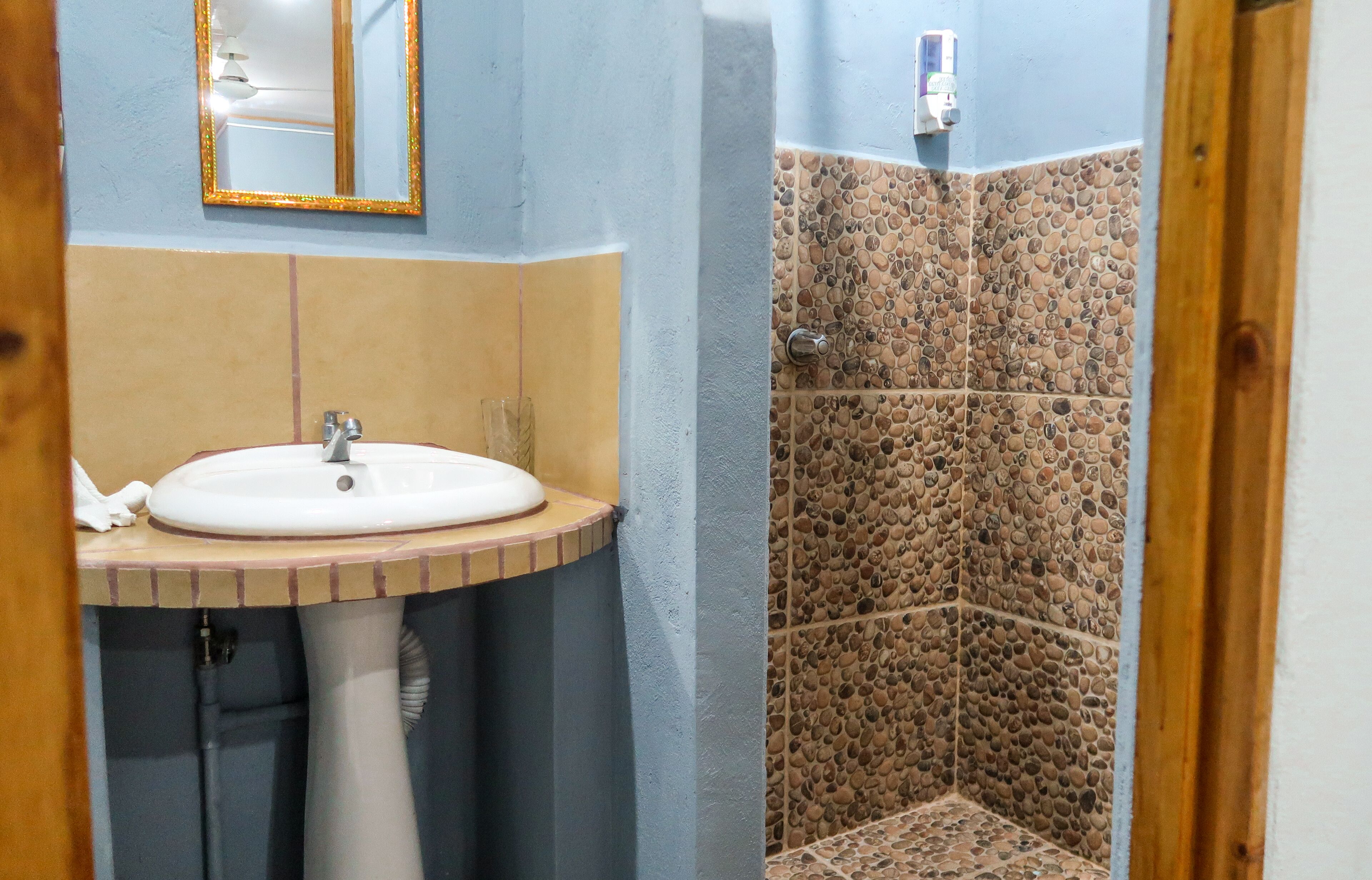 Casa de banho com lavatório, espelho e zona de duche com azulejos de pedra.