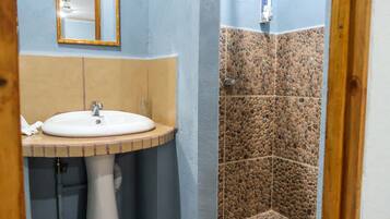 Casa de banho com lavatório, espelho e zona de duche com azulejos de pedra.