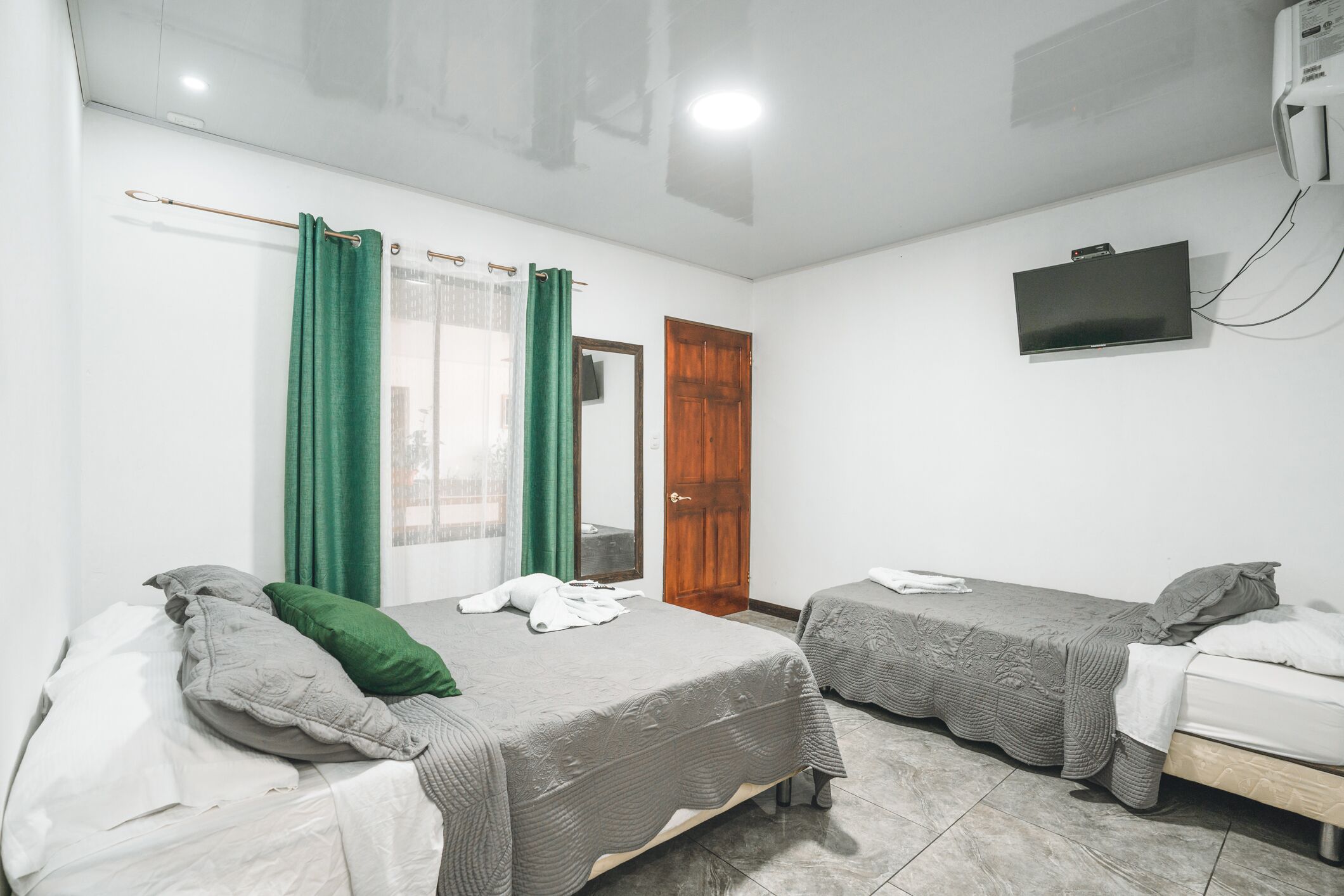 Une chambre avec deux lits, un téléviseur fixé au mur et une porte.