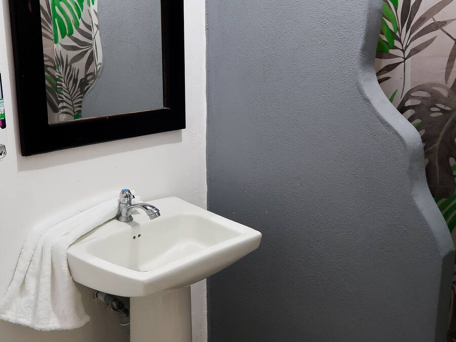 Un baño con un lavamanos blanco, un espejo y una pared gris con textura.