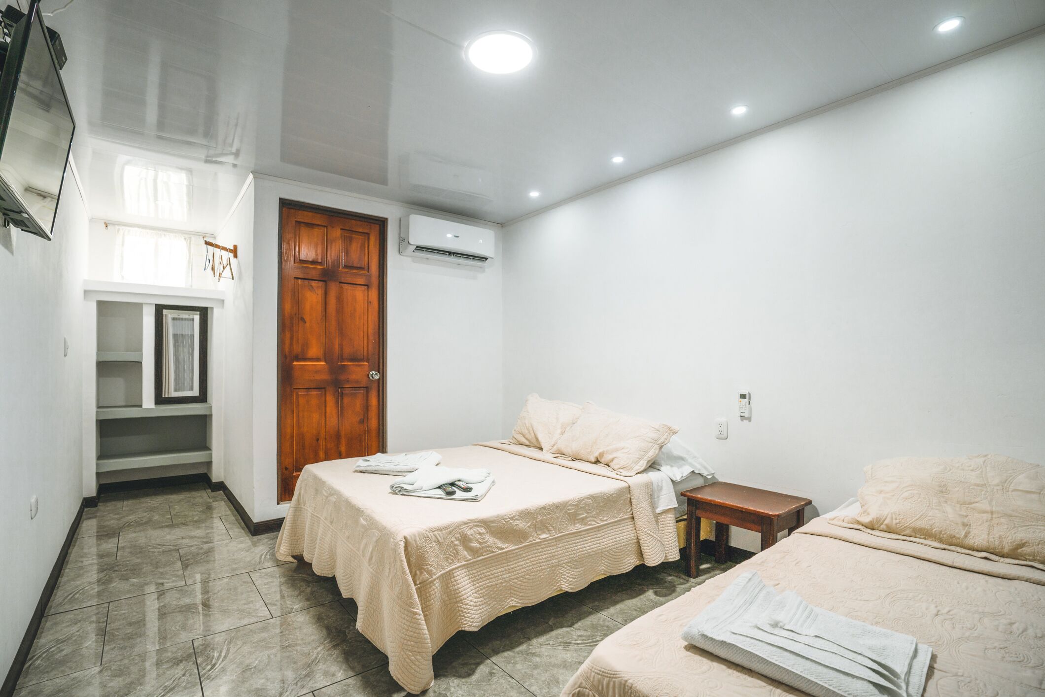 A bedroom with two beds, a wooden door, an air conditioning unit, and a small table.