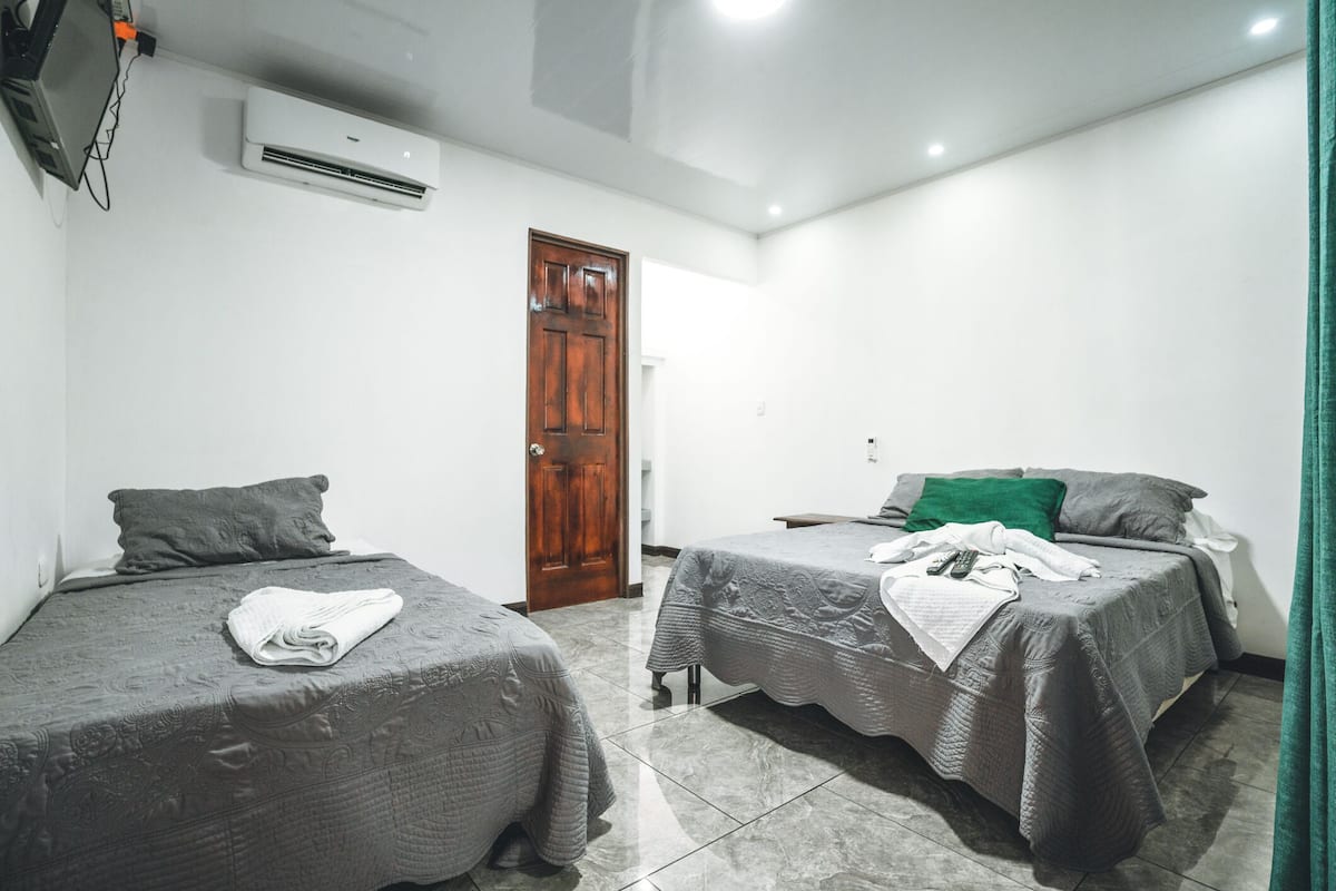 A room with two single beds, a wooden door, an air conditioning unit, and a green curtain.