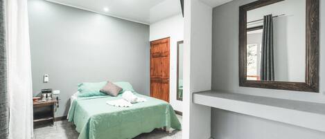A bedroom with a bed, a nightstand, a wooden door, and a mirror on the wall.