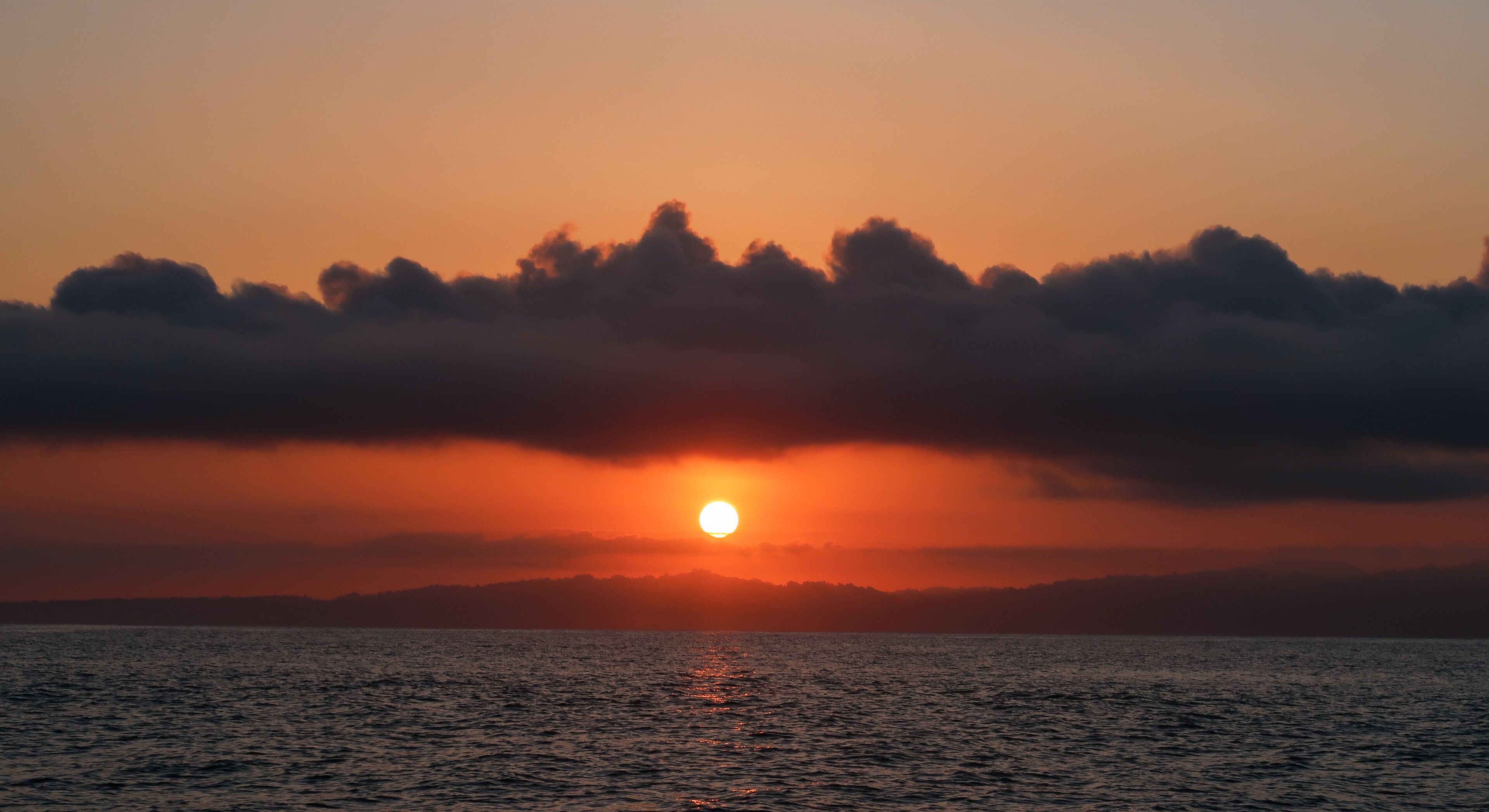 A sunset over a body of water with clouds in the foreground.