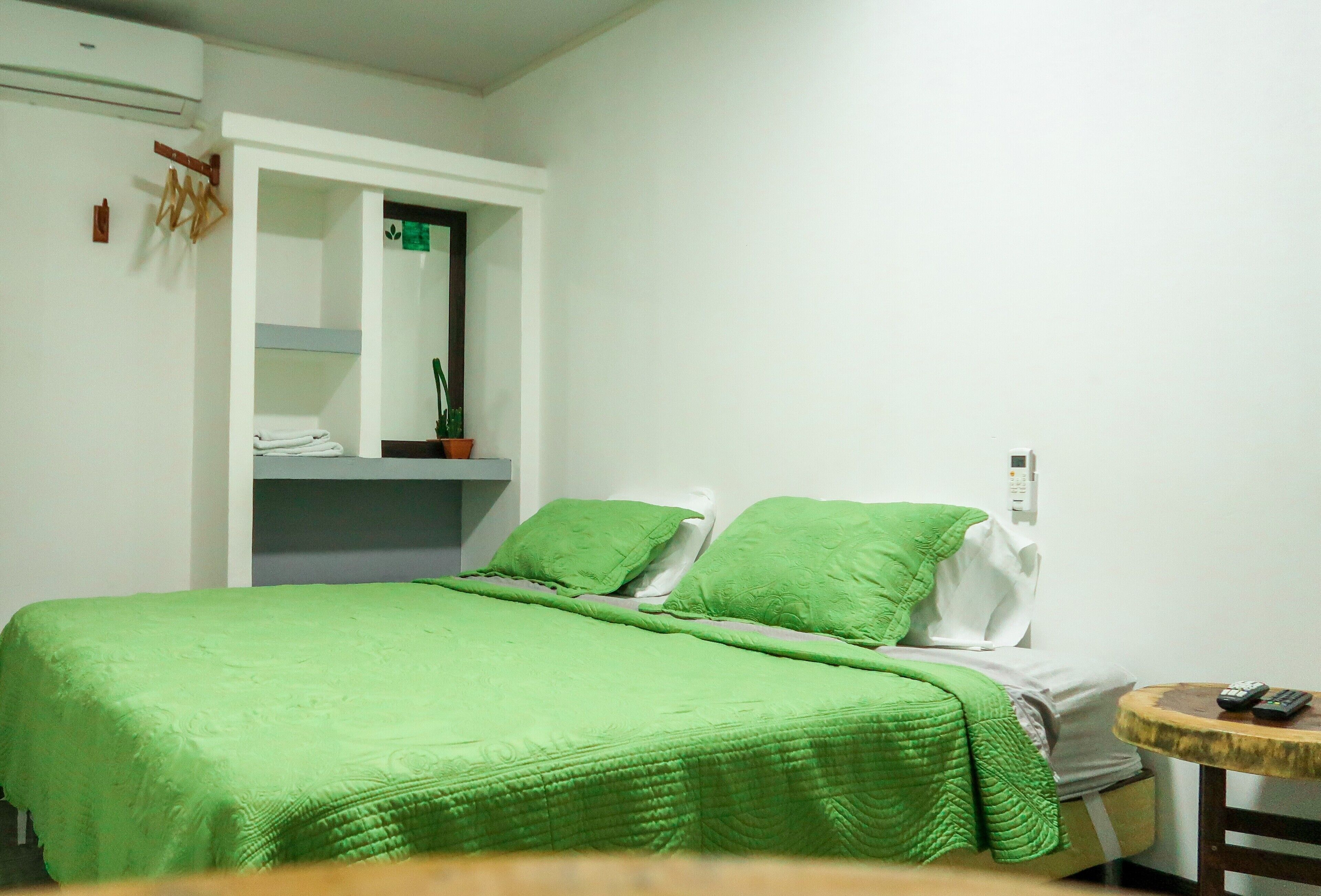 Een kamer met een bed, een kleintje tafel en een plank met opgevouwen kleding.