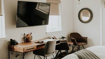 A hotel room with a wooden desk, two chairs, a television, a mirror, and a bed.