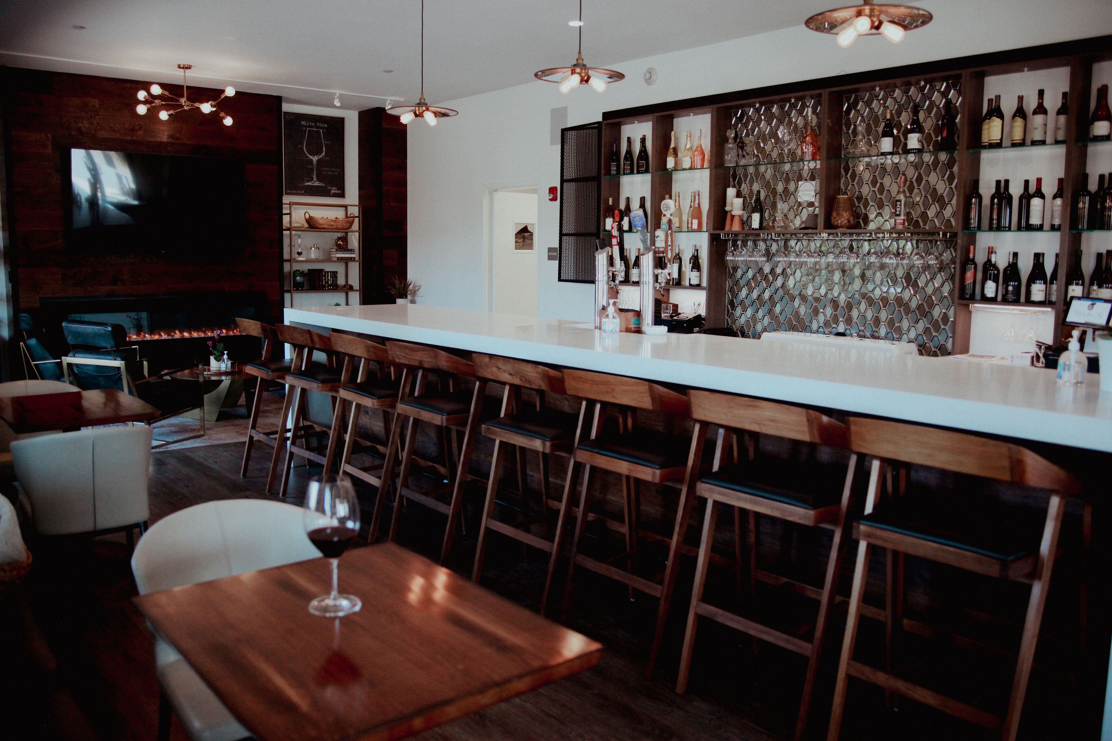 A bar area with wooden chairs, a long counter, and a wine rack filled with bottles.