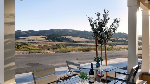 An outdoor patio with tables and chairs, a bottle of wine, and a glass of red wine. - Wine Stone Inn (Santa Maria)