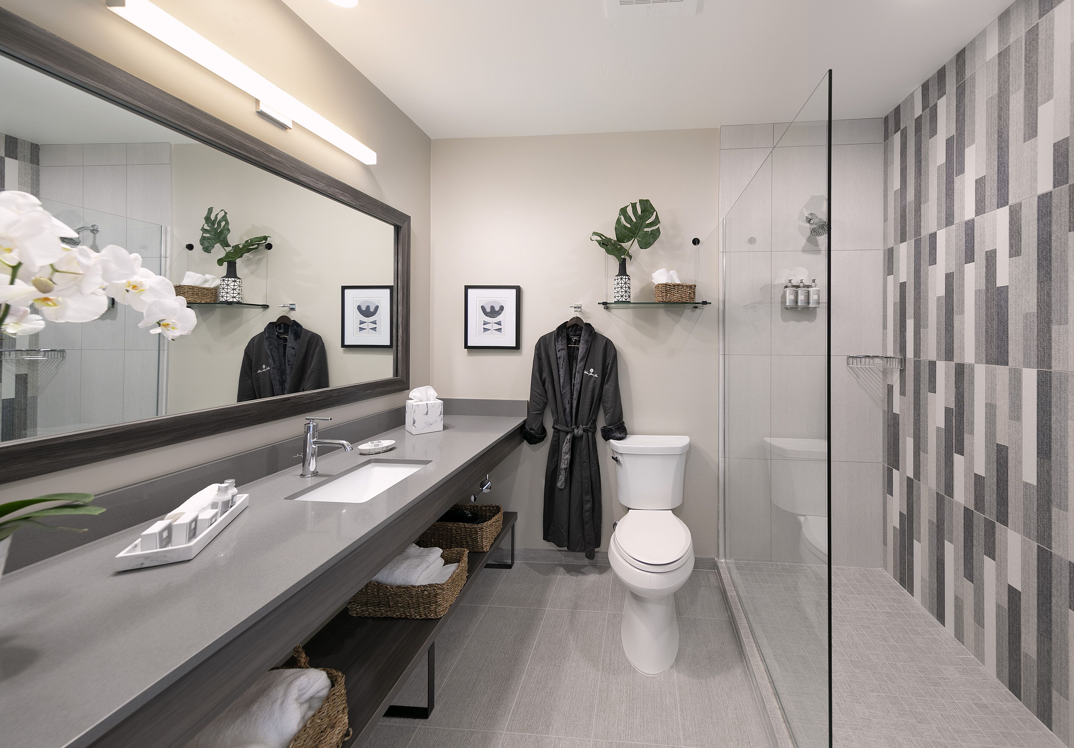 A modern bathroom with a large mirror, a white toilet, a shower area, and a vanity with a sink and towel racks.