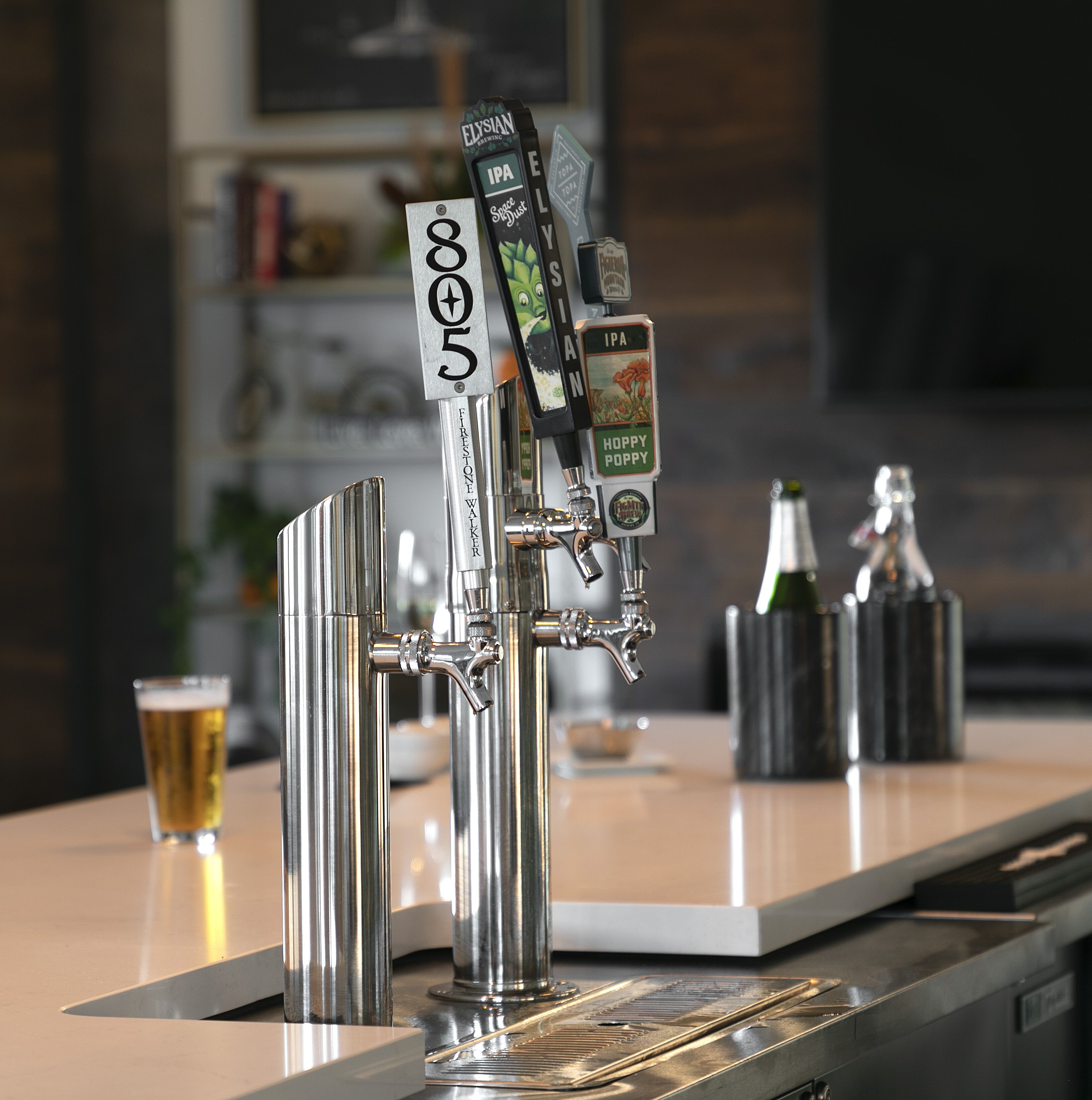 A tap with multiple beer options, a glass of beer, and two bottles on a bar counter.