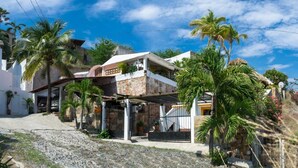 A two-story house with a stone facade, a covered porch, and a small garden with palm trees. - Casa Artista BnB Manzanillo (Manzanillo)