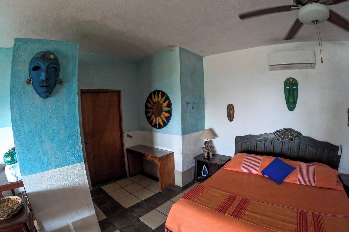 A bedroom with a bed, a ceiling fan, and a wall with decorative masks.