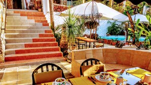 A dining area with a table set for two, a pool in the background, and a staircase leading to an upper level. - Casa Artista BnB Manzanillo (Manzanillo)