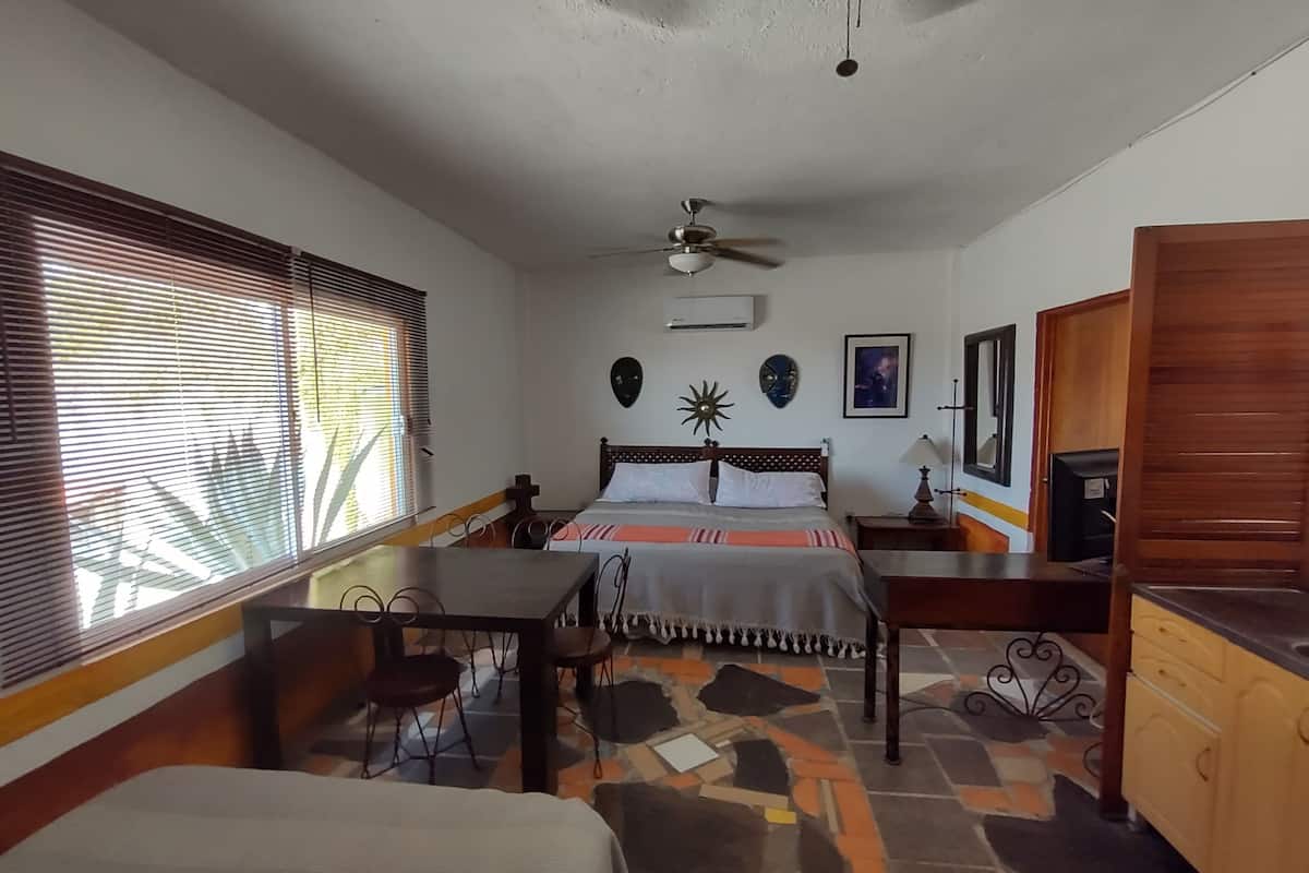 A bedroom with a bed, a desk, a chair, a ceiling fan, and a window with blinds.