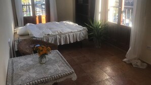 Habitación de hotel con una cama, una mesita con un florero, una planta en maceta y vistas al exterior a través de una ventana.