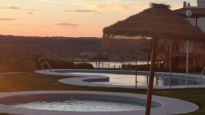 Un área de piscina con una estructura de techo de paja, una piscina pequeña y un espacio de descanso con barandilla de metal.
